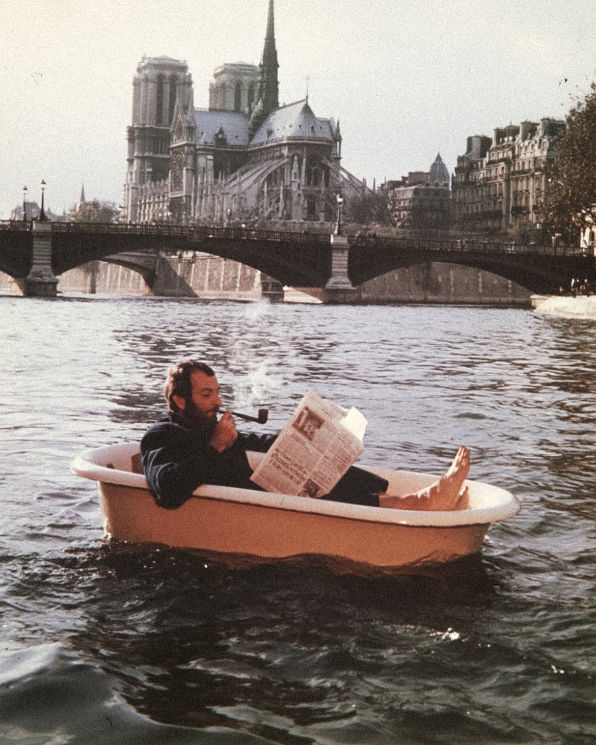 Un homme lit son journal, la pipe au bec, dans une baignoire qui flotte sur la Seine devant Notre-Dame