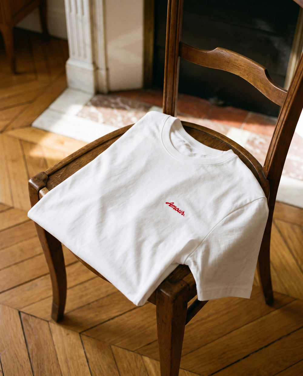 T-shirt brodé « Amour. » blanc plié sur une chaise en bois, appartement parisien